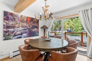 A dining area with a round table, brown chairs, a chandelier, and a large painting of a stream.