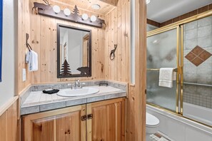 A wooden bathroom with a sink, mirror, and shower.