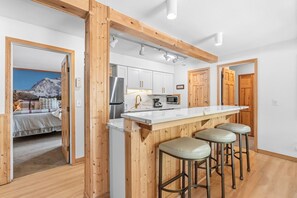 Een moderne keuken met een centraal kookeiland, houten balken en een paar barstoelen.
