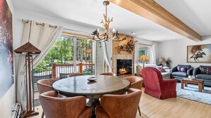 Ein Essbereich mit einem runden Tisch und Stühlen, einer Kandelaber, einem Kamin und einem Balkon mit Vorhängen.