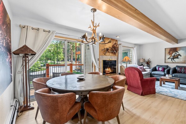 A dining area with a round table and chairs, a chandelier, a fireplace, and a balcony with curtains.