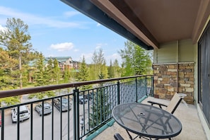 A balcony with a table and chairs, a stone wall, and a view of parked cars and buildings.