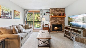 A living room with a sofa, coffee table, fireplace, TV, and artwork on the walls.
