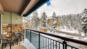 A balcony with a stone wall, two chairs, and a view of a snowy landscape with trees and buildings. - A Perfect Mountain Getaway On The Slopes near Hiking Trails in Summer TE315 (Breckenridge)