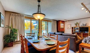 A dining area with a table set for four, a sofa, a television, and a bookshelf. - Unwind in Spacious Comfort. Retreat in an Unbeatable Breck Location TE511 (Breckenridge)