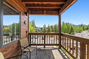 A wooden porch with a bench, a clock, and a view of a parking lot and trees.