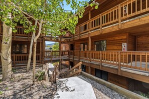 A wooden cabin with a balcony, a staircase, and a tree in the foreground.