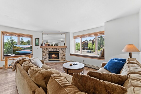 A modern living room with a stone fireplace, large windows, a television, and a sofa.