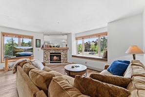 A modern living room with a stone fireplace, large windows, a television, and a sofa.