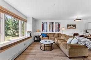 A living room with a large window, a sofa, a round coffee table, and a painting on the wall.