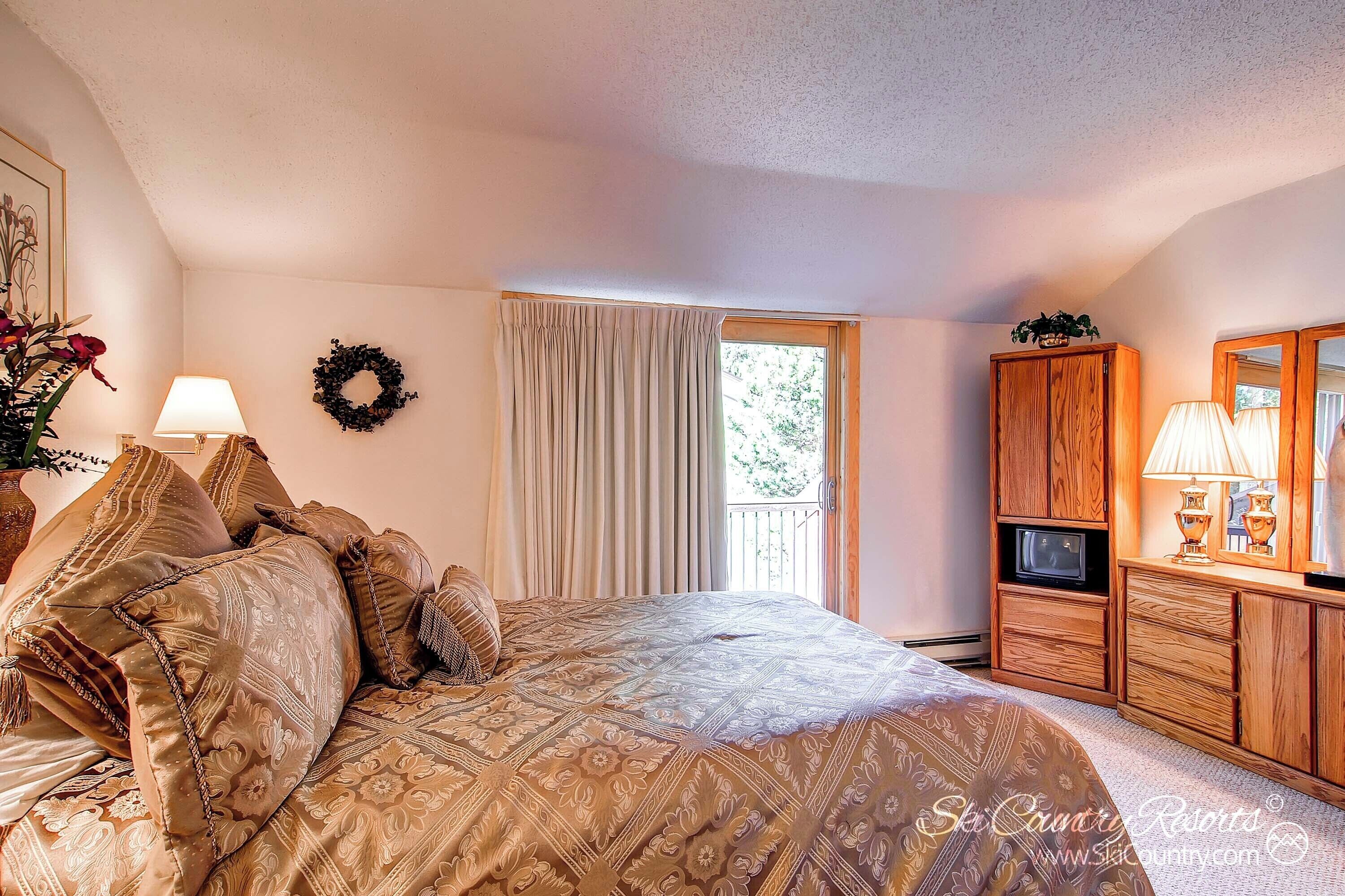 A bedroom with a large bed, a television, a wardrobe, and a window with curtains.
