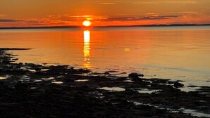Un atardecer sobre una superficie de agua tranquila con una costa rocosa.