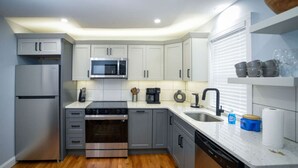 Cozinha moderna com armários cinza, eletrodomésticos em aço inoxidável, micro-ondas, fogão e lava-louças.