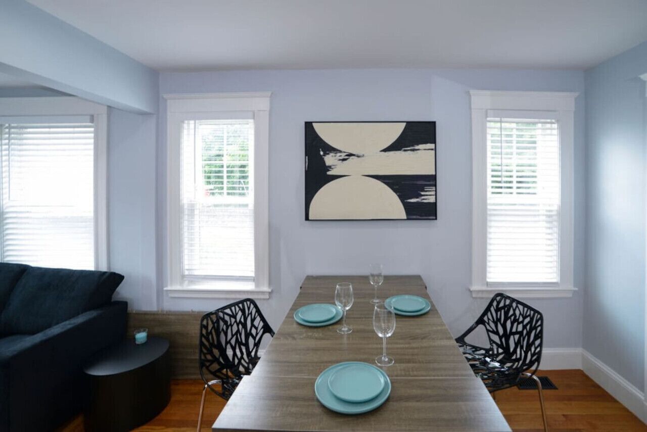A dining area with a wooden table set for four, two black chairs, and a large abstract painting on the wall.