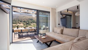 A modern living room with a large glass door leading to an outdoor dining area, a sofa, and a wooden coffee table. - Oasis Serenity,Serene,Nature views,Kids pool (Agouseliana)