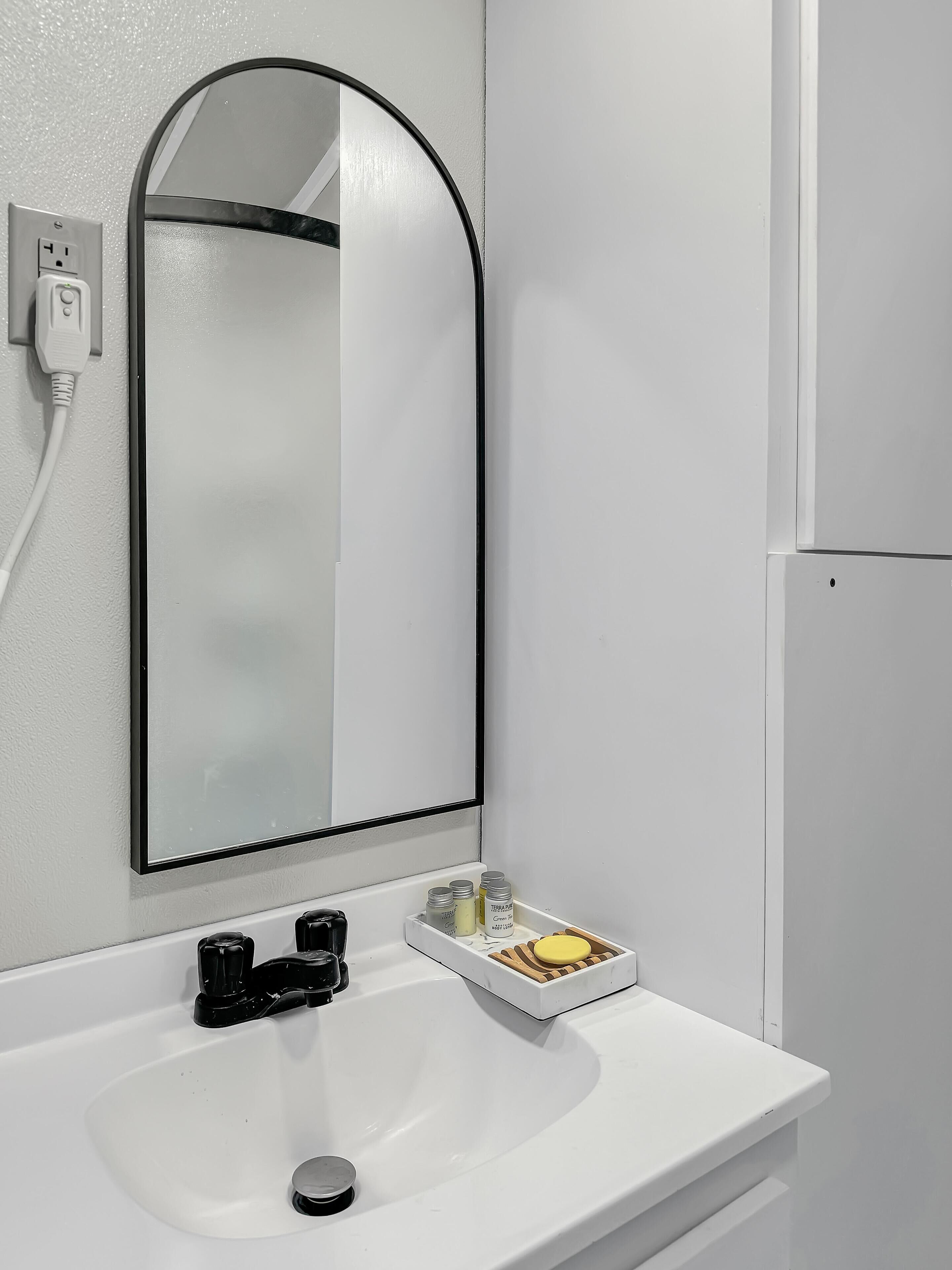 A bathroom with a white sink, a black faucet, a mirror with a black frame, and a small tray with toiletries.