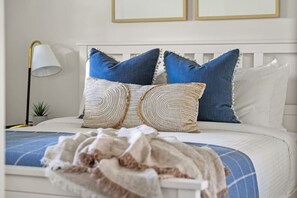 Ein Bett mit weißem Kopfteil, zwei blauen Kissen und einer gewebten Decke.