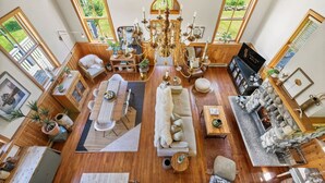 A spacious living room with a chandelier, wooden furniture, and large windows offering views of greenery. - Smith`s Church House | 1903 | Fireplace | Iconic (Wilmer)