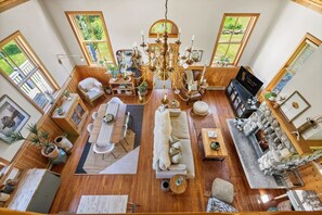 A spacious living room with a chandelier, wooden furniture, and large windows offering views of greenery. - Smith`s Church House | 1903 | Fireplace | Iconic (Wilmer)