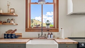A kitchen with a large window, wooden shelves, a sink, and a stove. - Smith`s Church House | 1903 | Fireplace | Iconic (Wilmer)