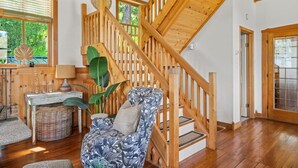 A wooden staircase leading to an upper level, a wicker basket, a patterned armchair, and a window with a view of greenery. - Smith`s Church House | 1903 | Fireplace | Iconic (Wilmer)