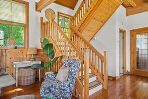 A wooden staircase leading to an upper level, a wicker basket, a patterned armchair, and a window with a view of greenery. - Smith`s Church House | 1903 | Fireplace | Iconic (Wilmer)