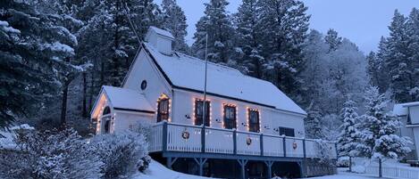 A snow-covered house with a balcony, surrounded by trees.