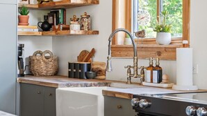 A kitchen with wooden shelves, a window with a clock, and a sink with a faucet. - Smith`s Church House | 1903 | Fireplace | Iconic (Wilmer)