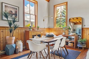 Un comedor con una mesa de madera, sillas blancas y un ventanal con vistas a zonas verdes.