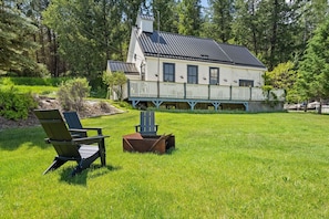 Una casa con porche, jardín y dos sillas Adirondack.
