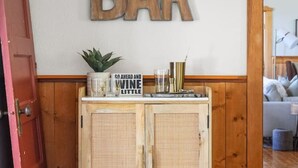 A wooden cabinet with a sign reading "BAR" above it, a potted plant, and a sign that says "GO AHEAD AND WINE LITTLE". - Smith`s Church House | 1903 | Fireplace | Iconic (Wilmer)