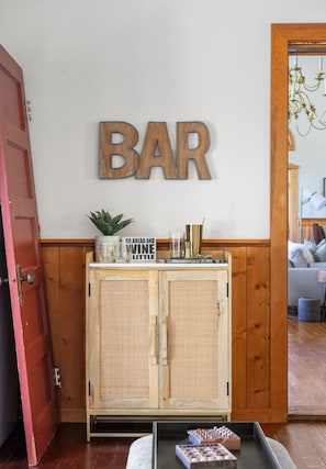 A wooden cabinet with a sign reading "BAR" above it, a potted plant, and a sign that says "GO AHEAD AND WINE LITTLE". - Smith`s Church House | 1903 | Fireplace | Iconic (Wilmer)