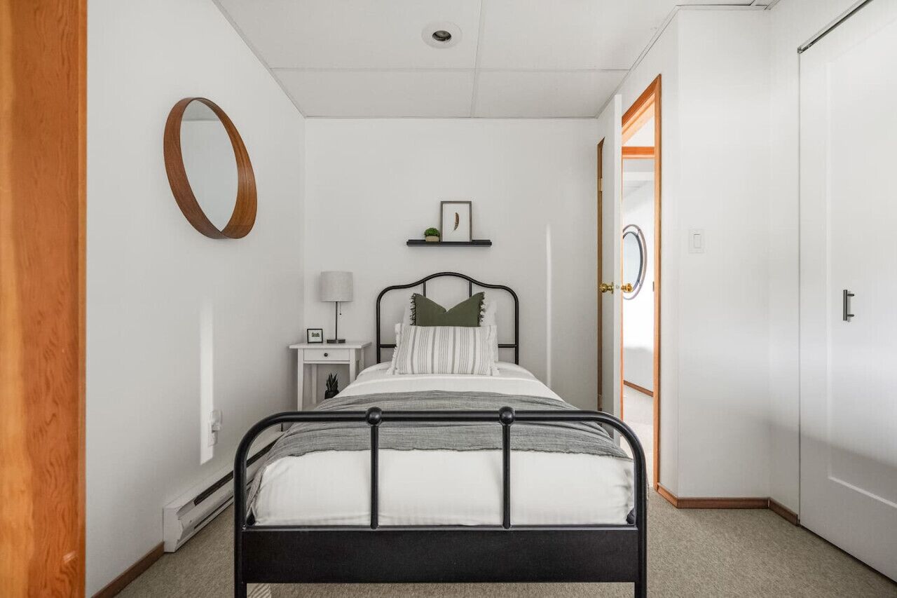 A bedroom with a bed, bedside table, lamp, and a door leading to another room.