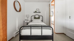 A bedroom with a bed, bedside table, lamp, and a door leading to another room. - Smith`s Church House | 1903 | Fireplace | Iconic (Wilmer)