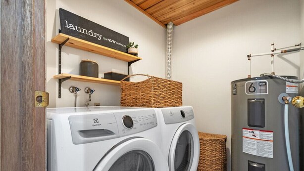 A laundry area with a washing machine, a dryer, and a water heater. There are shelves above the washing machine with a sign that reads "laundry the never ending." - Smith`s Church House | 1903 | Fireplace | Iconic (Wilmer)