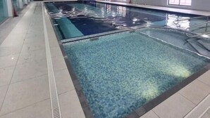 Une piscine dont le plafond est décoré d’une fresque représentant des arbres, avec un sol carrelé et une eau cristalline.