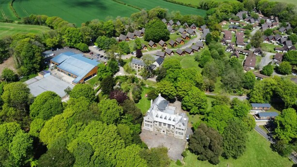 Vue aérienne d’un quartier résidentiel comprenant un grand domaine, plusieurs maisons et un parking.