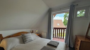 Une chambre avec un grand lit, une commode en bois et une vue sur l’extérieur par une fenêtre.