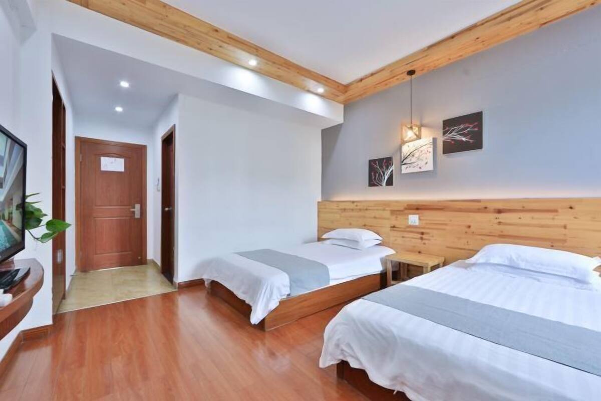 Ein Hotelzimmer mit zwei Betten, einem Holzkopfstück, einem kleinen Nachttisch, einem Fernseher und einer Pflanze.