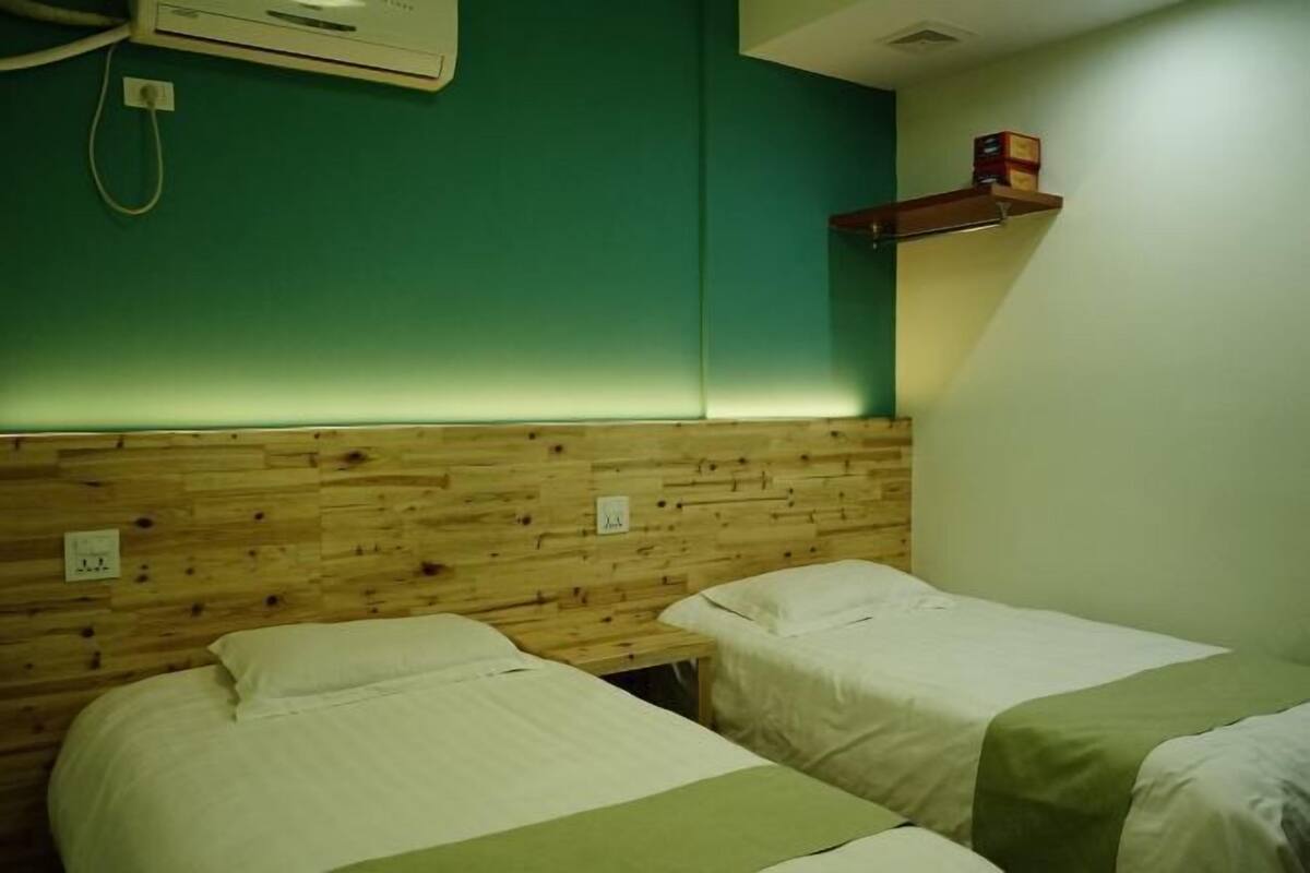 Ein Zimmer mit zwei Einzelbetten, einem Holzkopfstück, türkisblauen Wänden und einem Regal mit einer Schachtel.