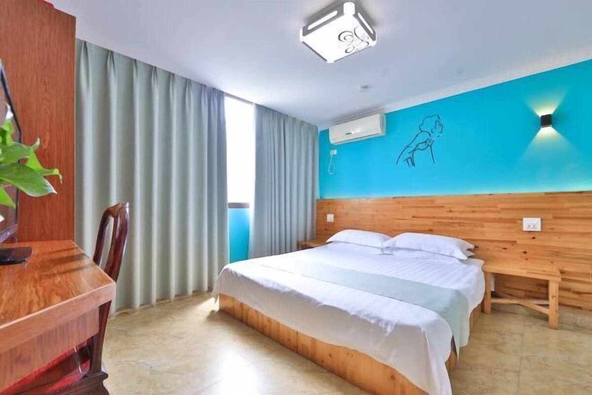 Ein Hotelzimmer mit einem hölzernen Bett, einem Schreibtisch und einem großen Fenster mit Vorhängen.
