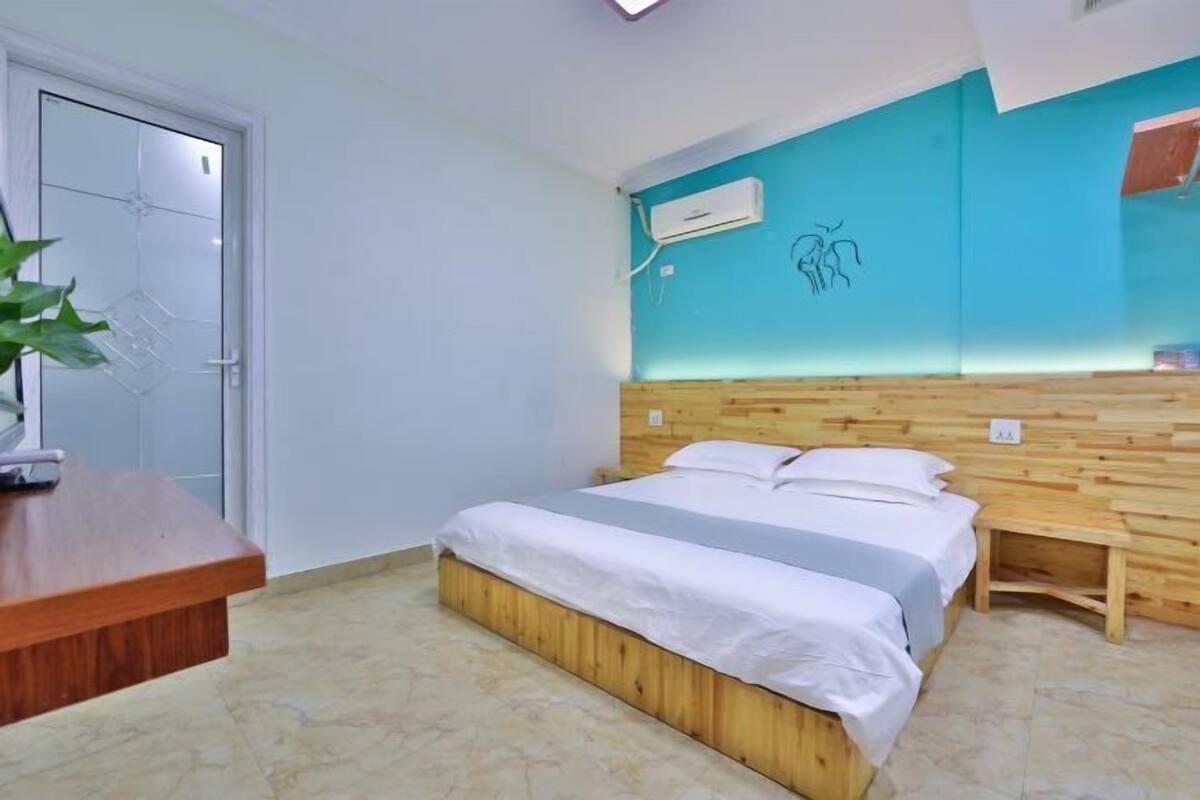 Ein Schlafzimmer mit einem hölzernen Kopfteil, einem Bett mit weißer Bettwäsche, einem kleinen Nachttisch, einer Topfpflanze und einer Wand-Klimaanlage.