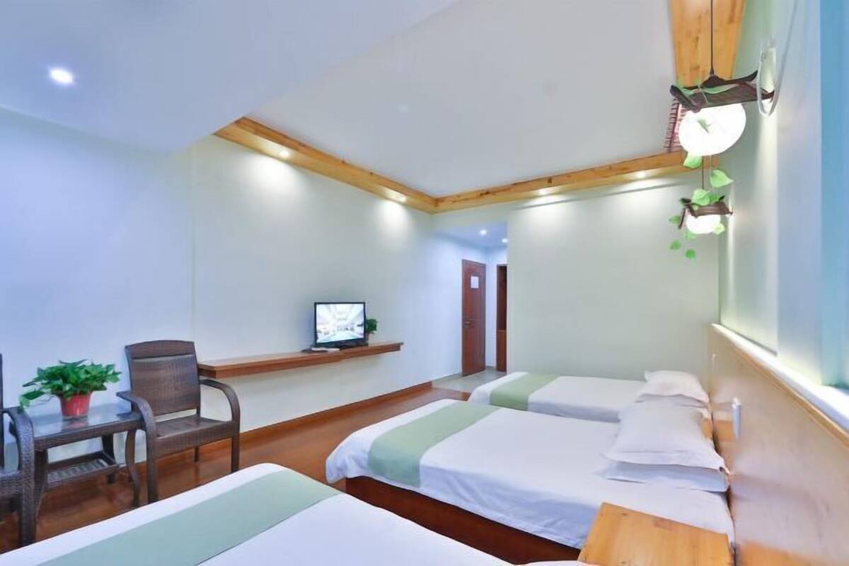 Ein Hotelzimmer mit zwei Betten, einem Schreibtisch mit Computer, einem Sessel und einem kleinen Tisch mit Pflanze.