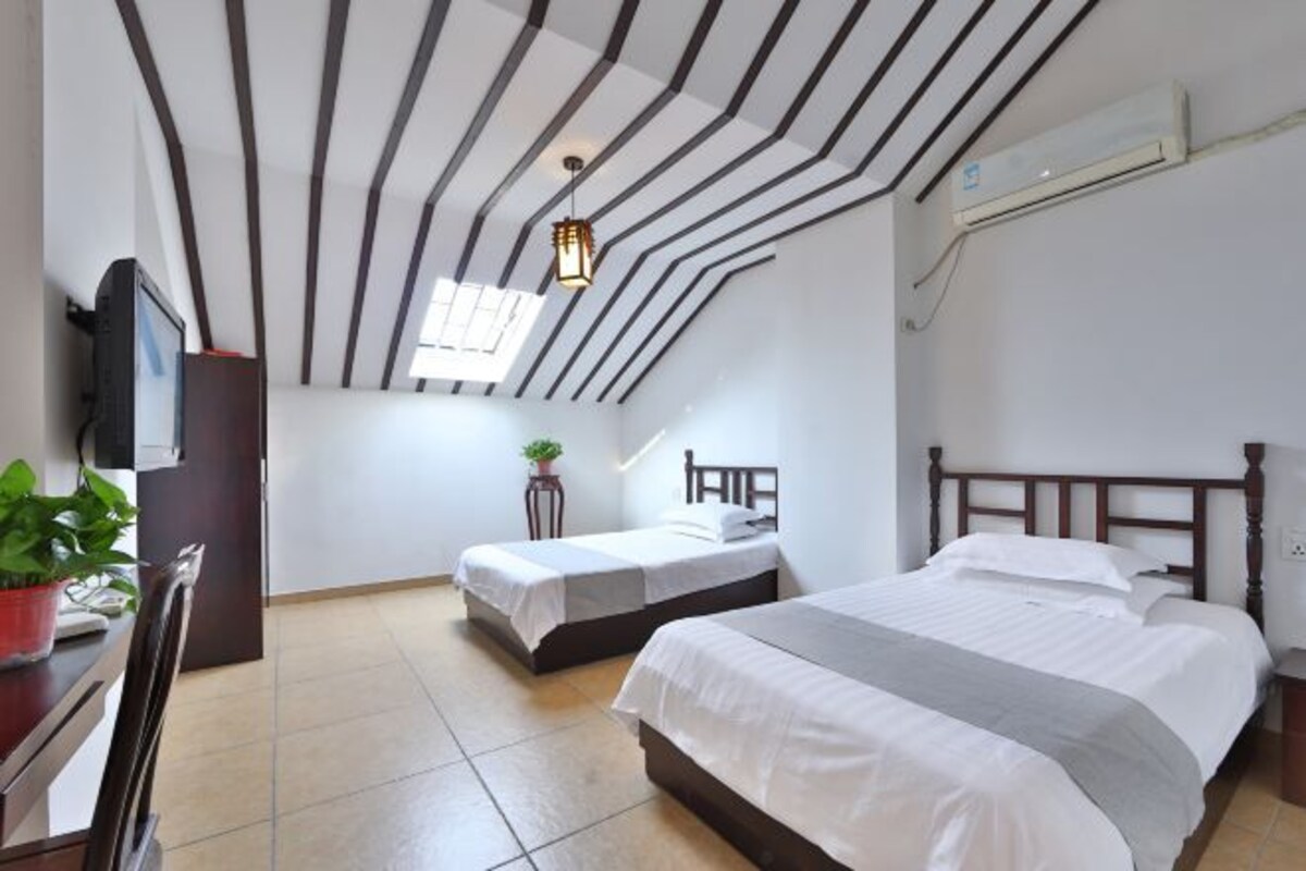 Une chambre à coucher avec un grand lit, un lit plus petit, un bureau avec un ordinateur, une plante et un plafond à rayures noires et blanches.