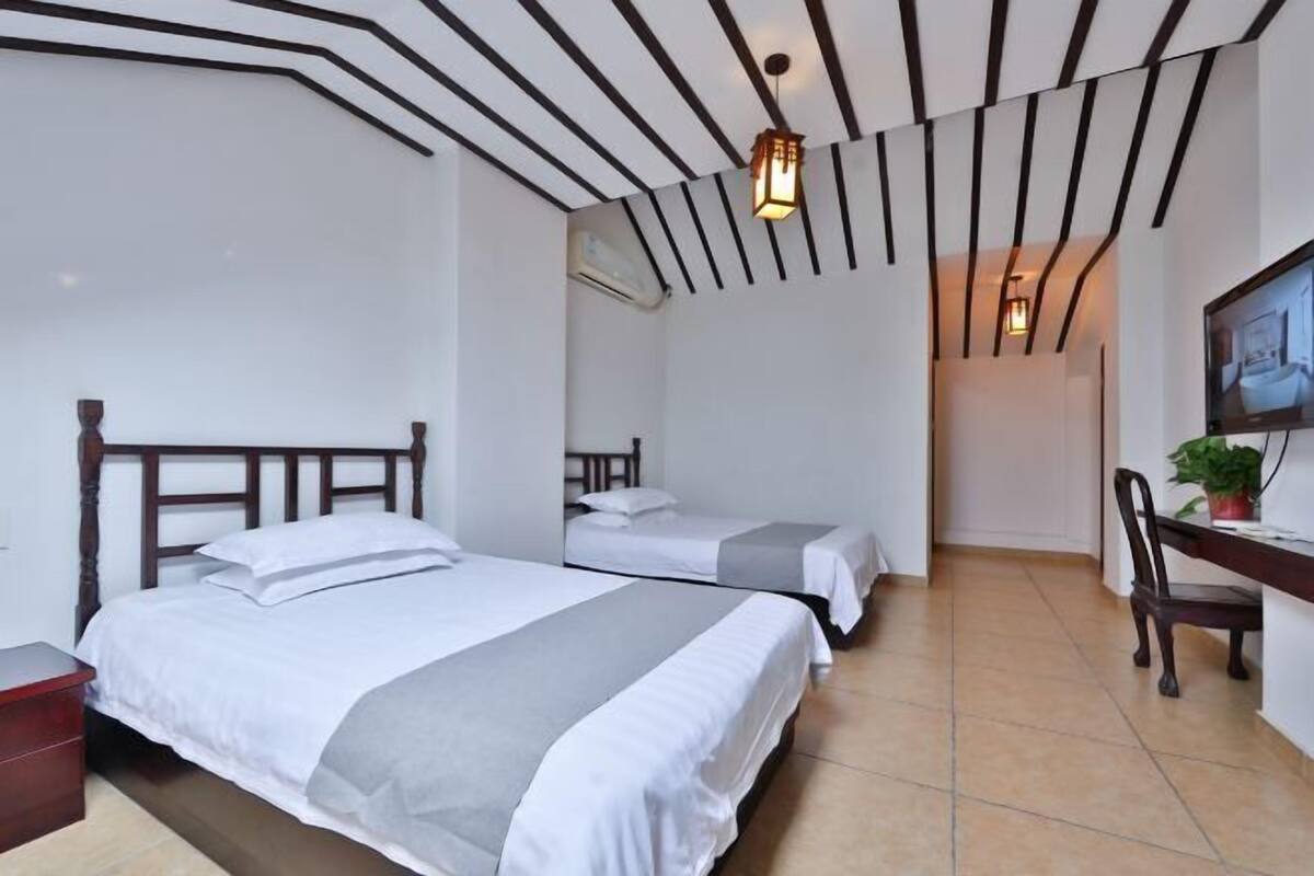 Ein Hotelzimmer mit zwei Betten, einem Schreibtisch, einem Stuhl, einem Fernseher und einer Decke mit schwarzen Balken.