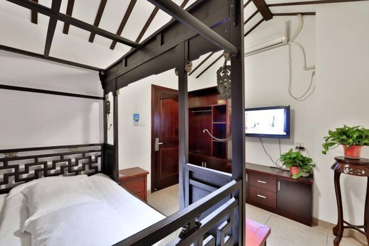 Ein Schlafzimmer mit einem Bett, einem Fernseher, einem Kleiderschrank und einem Schreibtisch mit Pflanze.