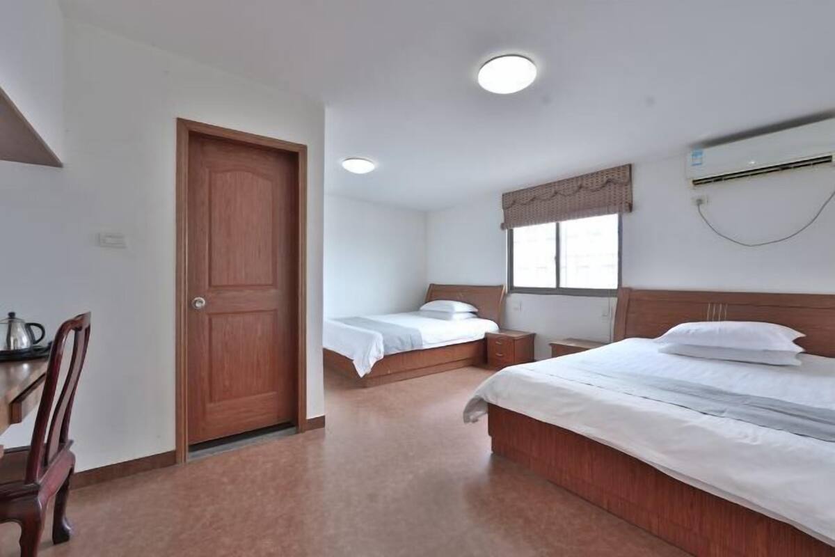 Ein Schlafzimmer mit zwei Betten, einer Holztür, einem Fenster mit Vorhängen und einer Klimaanlage.
