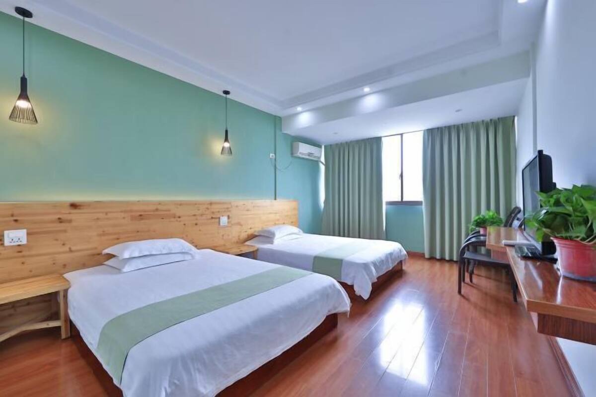 Ein Hotelzimmer mit zwei Betten, einem Holzkopfstück, einem Schreibtisch mit Stuhl, einem Fernseher und einem Fenster mit Vorhängen.