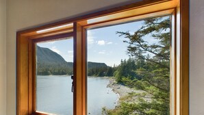 A window with a view of a lake and forested mountains. - Stunning Oceanfront Home w/ Mountain Views! (Juneau)
