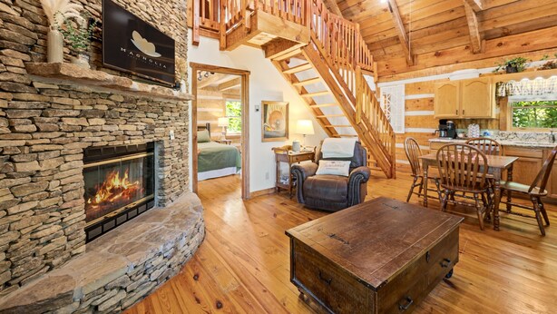 A cozy cabin interior with a stone fireplace, wooden staircase, and a dining area. - Relax on the Quiet Side – Hot Tub & Serenity! (Townsend)